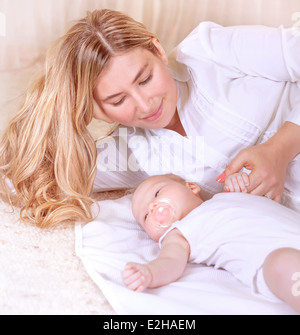 Glückliche junge Mutter liegend mit niedlichen Neugeborenen Baby zu Hause, genießen die ersten Tage der Elternschaft, liebevolle Familie Ausschreibung Stockfoto