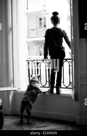 Mädchen stehen auf der Fensterbank mit Hund, beide mit Blick Stockfoto