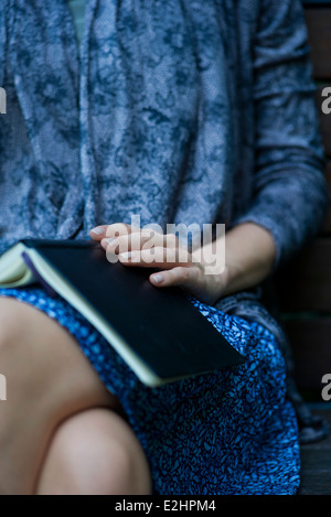 Frau sitzt mit offenen Buch ruht auf Schoß, beschnitten