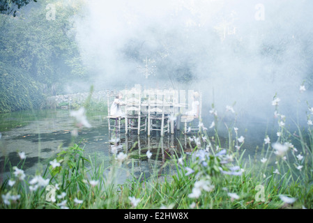 Kinder sitzen am Esstisch schwimmend auf Teich, umgeben von Rauch Stockfoto