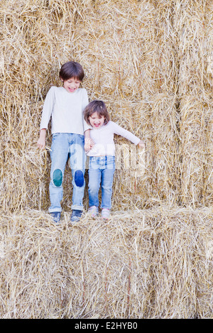 Junge Geschwister stehen auf Heuballen, Hand in Hand Stockfoto