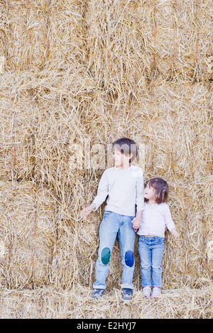 Junge Geschwister stehen auf Heuballen, Hand in Hand Stockfoto