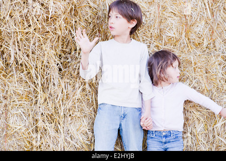 Junge Geschwister stehen auf Heuballen, Hand in Hand Stockfoto