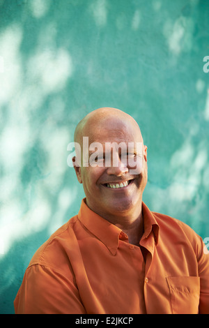 Porträt von Reifen kaukasischen Mann mit orangefarbenen t-Shirt im Park sitzen und Blick in die Kamera mit glücklichen Ausdruck Stockfoto