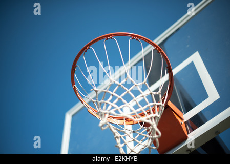Basketball Hoop Net gegen Blue Sky // ein orangener Basketballkorb mit transparentem Rückenbrett mit Netz gegen einen klaren blauen Himmel. Stockfoto