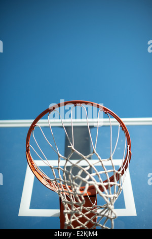 Basketballkorb Orange Netz Blauer Himmel | VEREINIGTE STAATEN — Eine Froschperspektive eines Outdoor-Basketballkorbs zeigt seinen orangefarbenen Stahlring und das Netz als Silhouette vor einem klaren blauen Himmel. Normgerechte Ringe sind orange lackiert und befinden sich 10 Fuß (3 m) über der Platzoberfläche, wobei das Netz den Fall des Balls durch den Korb verlangsamt. Das transparente Rückbrett dahinter ist ein übliches Design für öffentliche Außenplätze, das Sonnenlicht durchlässt und gleichzeitig Wetter Schäden widersteht. Stockfoto