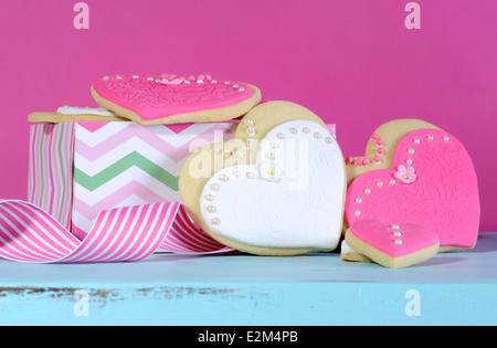 Rosa und weiße Braut und Brautjungfern Hochzeit Herz Form Cookies auf Vintage blaue Tabelle vor einem hellen heiß rosa Hintergrund. Stockfoto