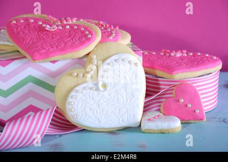 Rosa und weiße Braut und Brautjungfern Hochzeit Herz Form Cookies auf Vintage blaue Tabelle vor einem hellen heiß rosa Hintergrund. Stockfoto