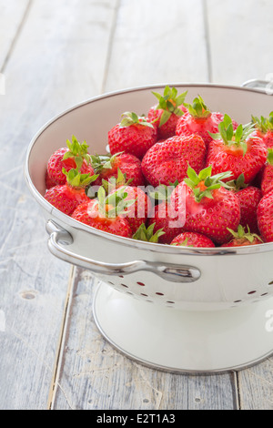 Frische Erdbeeren in einem weißen Emaille Sieb auf einem rustikalen Holztisch Stockfoto