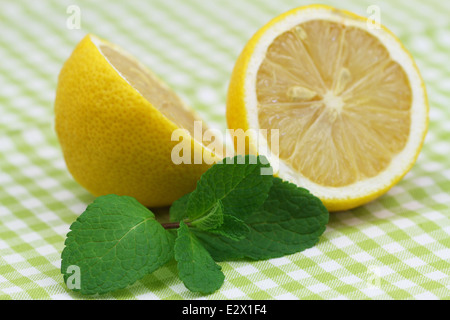 Zitrone-Hälften und frische Pfefferminzblätter auf kariertem Stoff Stockfoto
