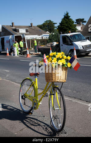 Frauen floral dekoriert gelb Fahrrad in York, Yorkshire, Großbritannien. Juni 2014. Wartungspersonal führt am Samstag Straßenreparaturen auf der Tour de France-Strecke durch. Insgesamt £4 Millionen wurden von acht Yorkshire Councils zugewiesen, um die Straßen der Region zu reparieren und die Route für die Tour de France im Juli vorzubereiten. Das Geld wird ausgegeben, um sicherzustellen, dass die 389 Kilometer Asphalt für die 2014 Tour Grand Abfahrt verwendet werden, wird Schlagloch frei sein. Die Strecke wird nun mit gelben Blumen, Flechtkörben und Fahrrädern gesäumt. Stockfoto