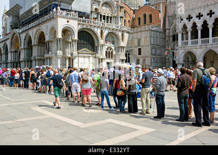 Lange Schlange für Sommertouristen, Leute in legerer Kleidung, die draußen Schlange stehen Italienischer Dogenpalast in Richtung der geschäftigen historischen Markusbasilika Venedig Venetien Italien Stockfoto