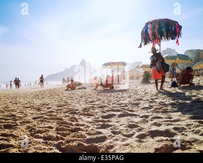 RIO DE JANEIRO, Brasilien - 5. März 2013: Anbieter verkaufen Bikinis geht vorbei an Beachgoers Sonnenbaden am Ipanema Strand Rio de Janeiro Stockfoto