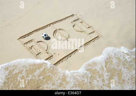Einfache Strichzeichnung Fußball Spielfeld Taktik Board mit Fußball im Sand am brasilianischen Strand mit ankommenden Welle Stockfoto