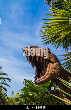 Die verrosteten Kopf einer T-Rex Dinosaurier Skulptur zeichnet sich unter Palmen. Stockfoto