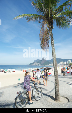 RIO DE JANEIRO, Brasilien - 1. April 2014: Frau fährt Fahrrad entlang der Promenade am Arpoador einen Blick auf den Strand von Ipanema. Stockfoto