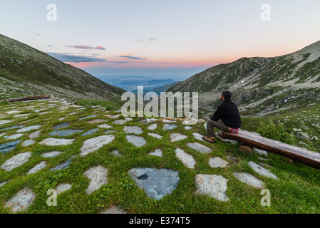Männliche Wanderer auf einer Bank sitzen und betrachten kurz nach Sonnenuntergang. Stockfoto