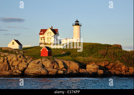 Maines Nubble Leuchtturm leuchtet in warmem Gelb wie die Sonne am Horizont vor der Lichtquelle. Stockfoto