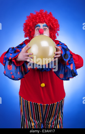 Clown mit einem Ballon in Händen auf blauem Hintergrund. Professionelle Beleuchtung. Humor. Make-up. Glück Stockfoto