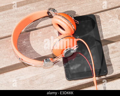 Lebendige orange Kopfhörer und schwarz tablet-pc auf Holzbank für mobile Sprachenlernen oder Fernstudium Stockfoto