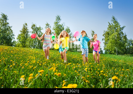 Glückliche Kinder laufen mit Luftballons im Sommer Stockfoto