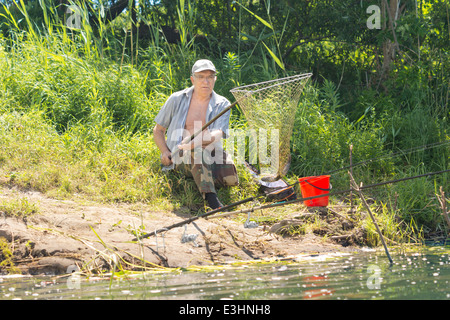 Senioren Behinderte ein vierbeiniger Fischer einen Fisch in einem langstieligen Fischnetz landen, da er einen Tag mit Angeln am Ufer eines Sees verbringt Stockfoto