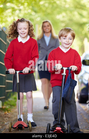 Kinder reiten Roller auf dem Weg zur Schule mit Mutter Stockfoto