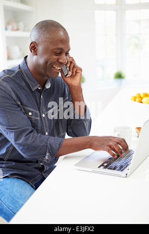 Mann mit Laptop und Gespräch am Telefon In der Küche zu Hause Stockfoto