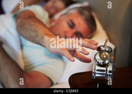 Paar im Bett mit Mann bis Wecker ausschalten Stockfoto