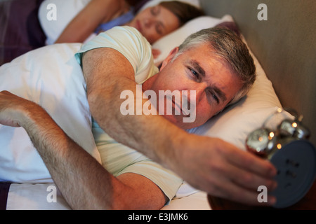 Paar im Bett mit Mann bis Wecker ausschalten Stockfoto