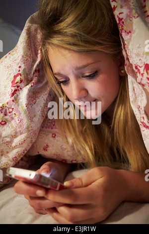 Unglückliche Teenager-Mädchen senden SMS, während im Bett liegend Stockfoto