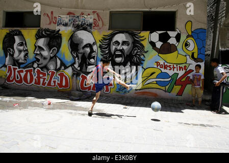 Gaza, Gazastreifen, Palästinensische Gebiete. 23. Juni 2014. Einen palästinensischen Jungen einem Ball vor Graffiti Wand Wandmalereien Fußballer spielen die Teilnehmer 2014 World Cup Brasilien (LtoR) Portugals Cristiano Ronaldo, Argentiniens Lionel Messi, Niederlande Arjen Robben und Italiens Andrea Pirlo, im Flüchtlingslager Khan Yunis im südlichen Gazastreifen. am 23. Juni 2014. © Ari Rahim Khatib/NurPhoto/ZUMAPRESS.com/Alamy Live-Nachrichten Stockfoto