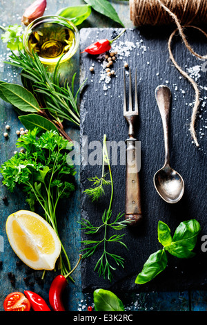 Essen-Hintergrund, mit Kräutern, Gewürzen, Olivenöl, Salz, Zitronen und Gemüse. Schiefer und Holz Hintergrund. Stockfoto