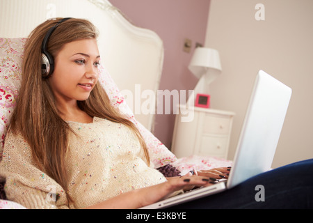 Teenager-Mädchen auf Bett mit Laptop mit Kopfhörern Stockfoto