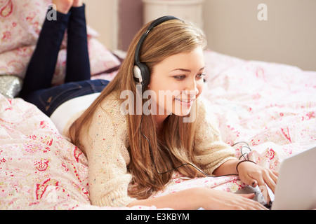 Teenager-Mädchen auf Bett mit Laptop mit Kopfhörern Stockfoto