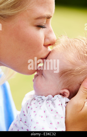 Liebevolle Mutter küssen Baby Tochter im Garten Stockfoto