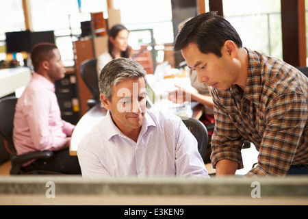 Zwei Kollegen, die Arbeiten am Schreibtisch mit treffen im Hintergrund Stockfoto