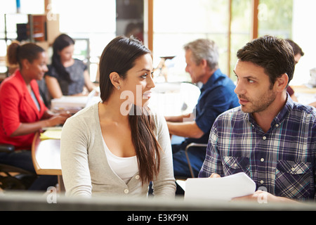 Zwei Kollegen, die Arbeiten am Schreibtisch mit treffen im Hintergrund Stockfoto