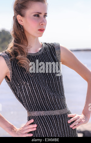 Modebewusste Frau am Ufer, sie trägt schwarzes Kleid mit einem Streifen Stockfoto