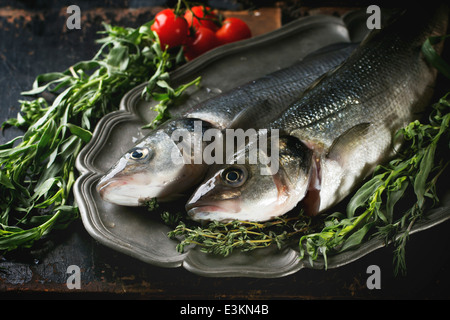 Schlepptau Rohfisch Wolfsbarsch serviert mit Kräutern und Kirschtomaten auf Vintage Platte über schwarzer Holztisch Stockfoto