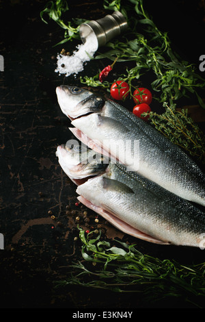 Abschleppen von rohem Fisch Wolfsbarsch mit Kräutern, Meersalz und Kirschtomaten auf schwarzer Holztisch serviert Stockfoto