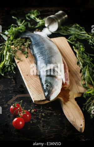 Roher Fisch Wolfsbarsch mit Kräutern, Meersalz und Kirschtomaten auf Holzbrett über schwarzer Holztisch gedient. Stockfoto