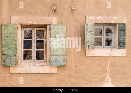 Windows mit grünen Fensterläden. Ein paar Fenster klein auf eine tan farbige Stuck Wand mit rauer, die grüne Fensterläden öffnen. Stockfoto