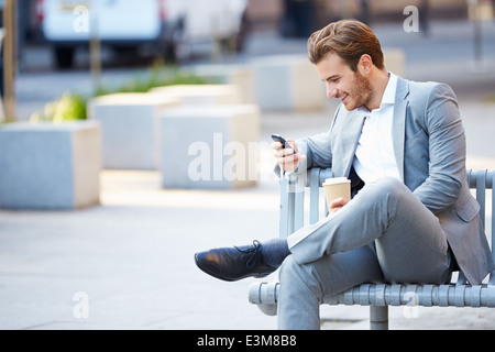 Geschäftsmann auf Parkbank mit Kaffee mit Handy Stockfoto