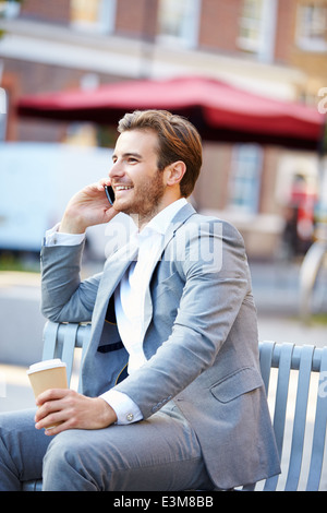 Geschäftsmann auf Parkbank mit Kaffee mit Handy Stockfoto