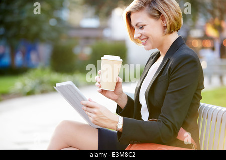 Geschäftsfrau auf Parkbank mit Kaffee mit Digital-Tablette Stockfoto