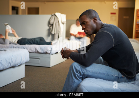 Männer sitzen auf den Betten im Obdachlosenheim Stockfoto