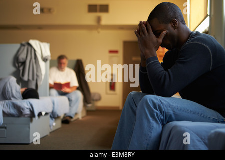 Männer sitzen auf den Betten im Obdachlosenheim Stockfoto