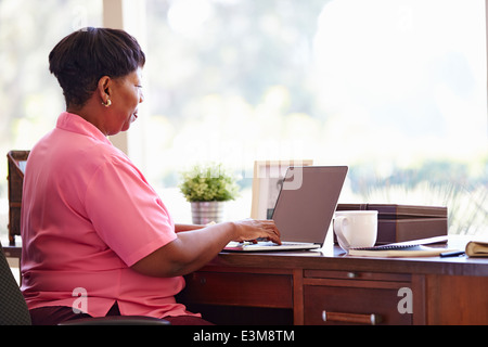 Reife Frau mit Laptop am Schreibtisch zu Hause Stockfoto