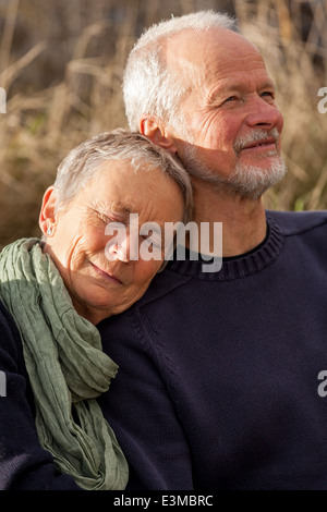 gerne älteres Paar gemeinsam entspannen in der Sonne auf einer Holzbank in der Landschaft mit einer stützenden voller Länge auf Stockfoto